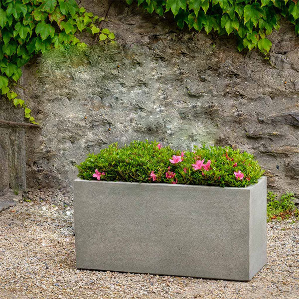 Concrete Planters Collection Image of Metro Box Planter on gravel filled with pink flowers.