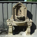 Anduze Wall Fountain Tall on concrete against gray fence.
