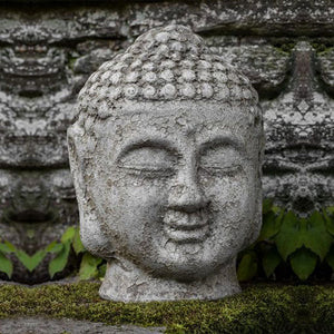 Angkor Buddha Head Small on grass against concrete wall