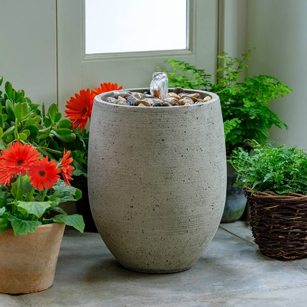 Bebel Pebble Fountain on concrete beside orange flowers