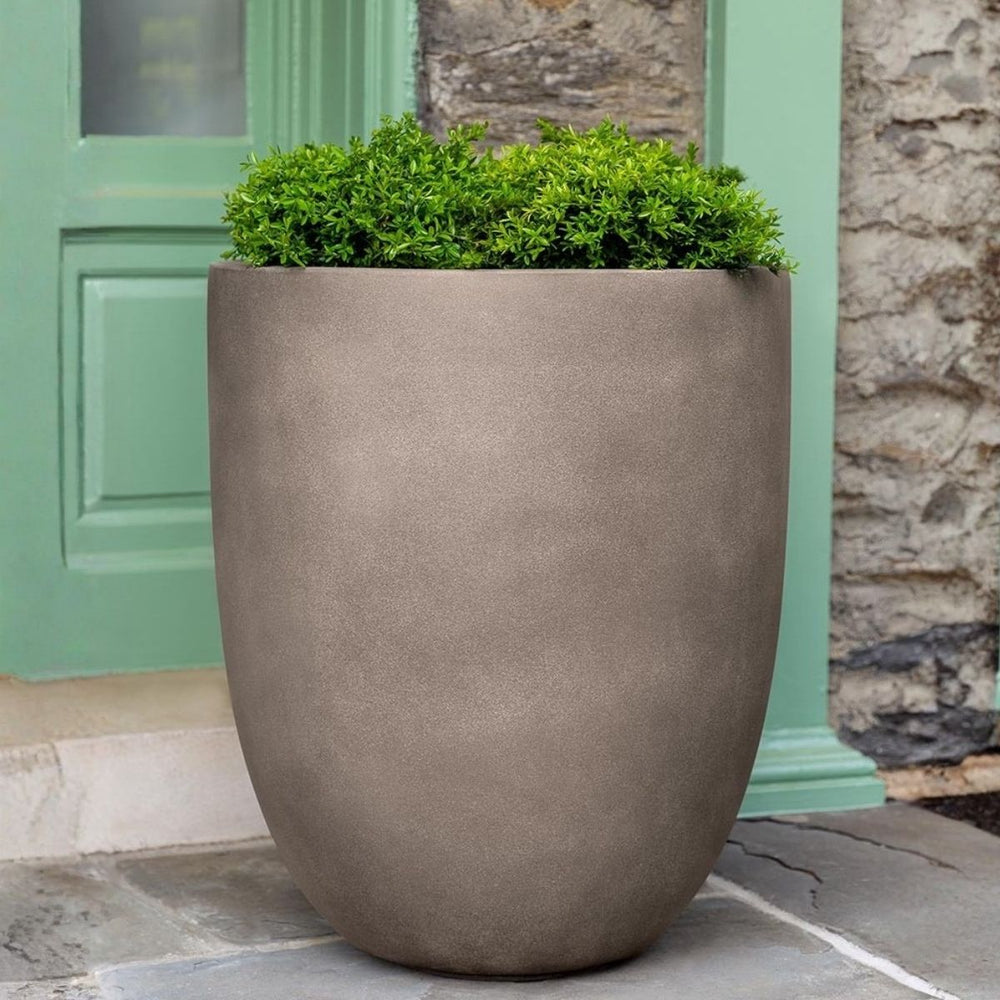 Bradford Planter Extra Large in riverstone premium lite color on concrete filled with plants.