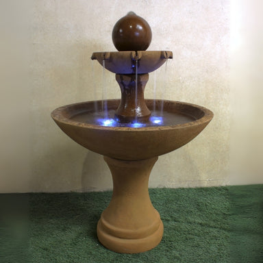 Circen Two Tier Fountain on grass against brown background.