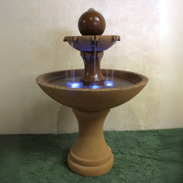 Circen Two Tier Fountain on grass against brown background.