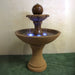 Circen Two Tier Fountain on grass against brown background.