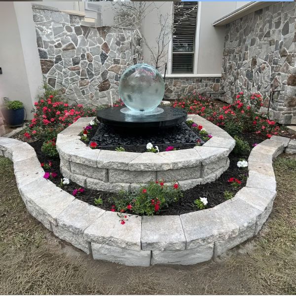 Crystal Sphere Fountain Kit installed in round stone bed with colorful flowers in front of home with stone exterior