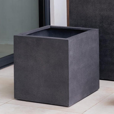 Farnley Planter 3636 S/1 in charcoal premium lite on concrete beside glass wall.