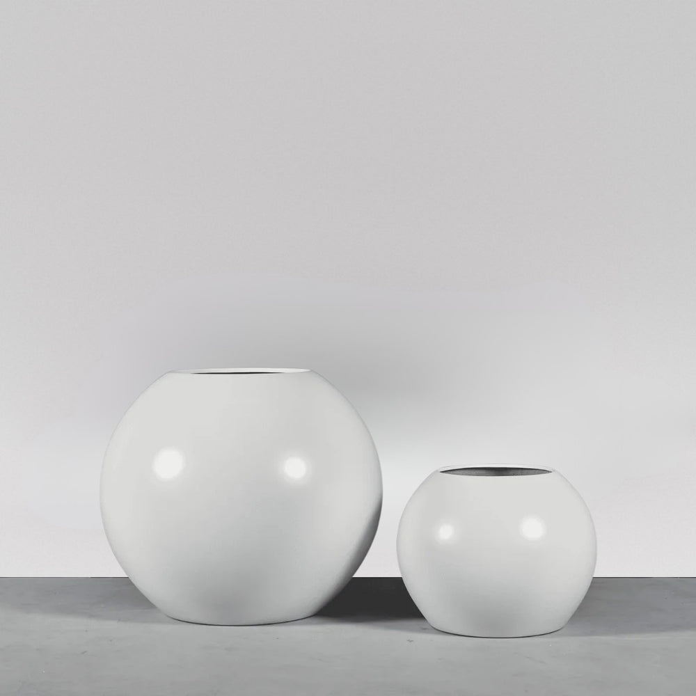 Globe Fiberglass Planter on concrete against gray background.