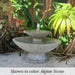Jensen Oval Fountain on concrete against green plants. 