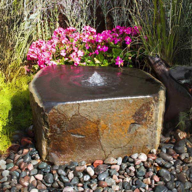 Keki Fountain Kit on gravel beside pink flowers