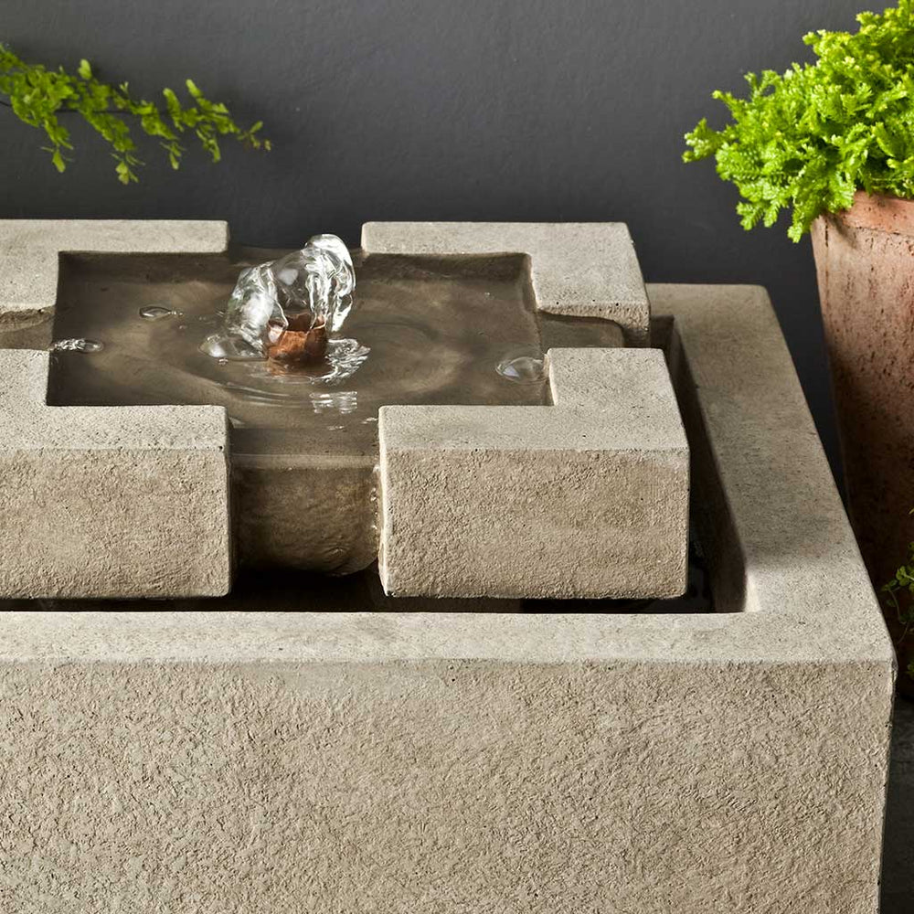 M-Series Escala Fountain on concrete beside green plants upclose.