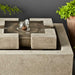 M-Series Escala Fountain on concrete beside green plants upclose.