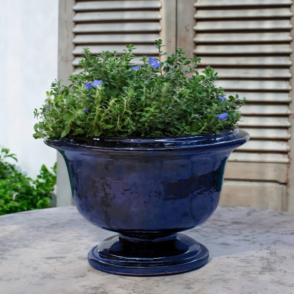 Margaux Urn Planter in riviera blue color on table filled with plants.