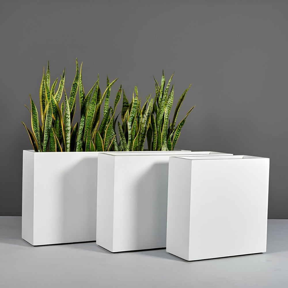 Milano Narrow Rectangle Planter against gray wall filled with plants. 