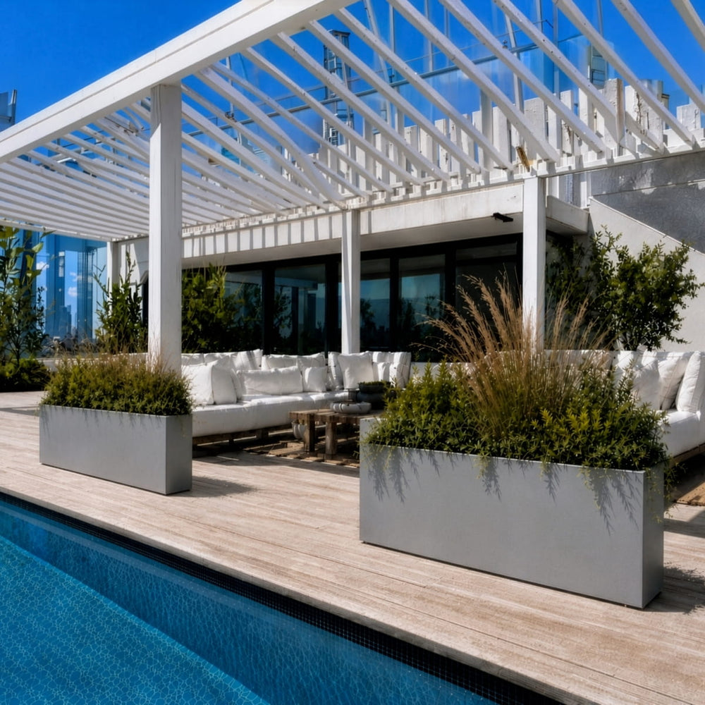 White Milano rectangular planters with ornamental grasses and greenery beside a luxury poolside pergola seating area.