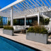 White Milano rectangular planters with ornamental grasses and greenery beside a luxury poolside pergola seating area.