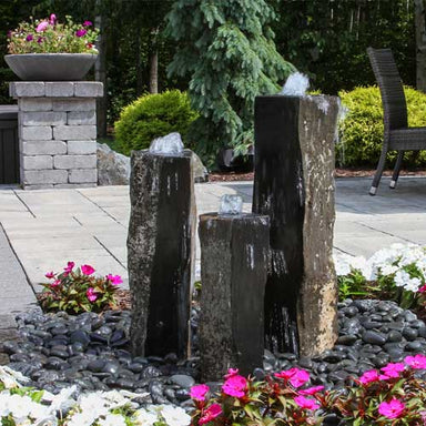 One Side Polished Basalt Fountain Kit on black pebbles surrounded with pink and white flowers