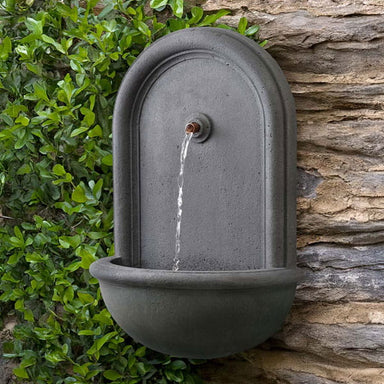 Perugia Wall Fountain in action beside green leaves.