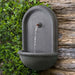 Perugia Wall Fountain in action beside green leaves.