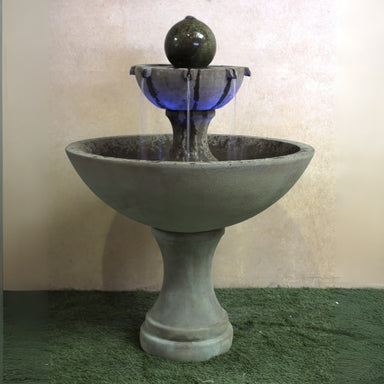 Ronde Two Tier Fountain on grass against brown background.