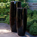 Sabine Planter, Tall - Flint - S/1 on concrete beside plants