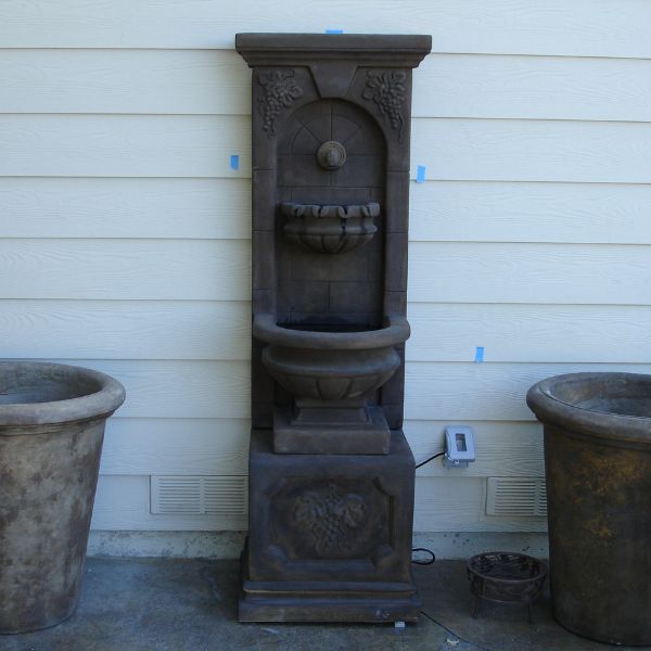 St. Helena Fountain with base concrete spout on concrete against white wall.