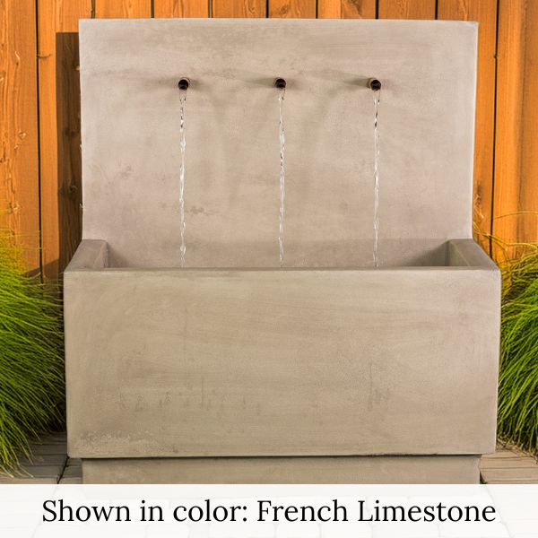 Tribus Wall Fountain in french limestone color agaisnt wooden fence.