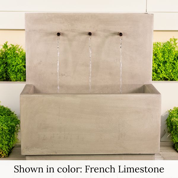 Tribus Wall Fountain in french limestone color in action beside green plants.