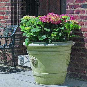 Certosa Medallion Planter filled with flowers against red brick wall