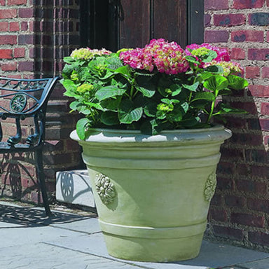 Certosa Medallion Planter filled with flowers against red brick wall