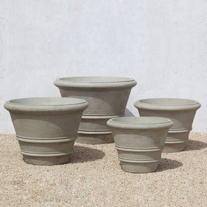 Classic Rolled Rim 24 inch Planter with three different sized planters on gravel against cream wall