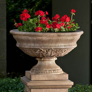Coachhouse Urn on pedestal filled with red flowers on gravel in backyard