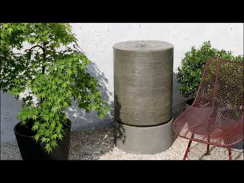 Campania Large Cylinder Fountain running on gravel patio next to plants