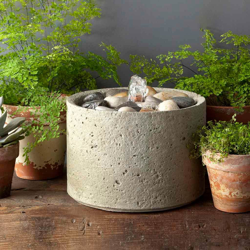 M-Series Pebble Fountain on table beside green plants