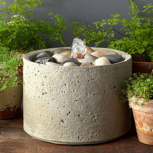 M-Series Pebble Fountain on table beside green plants
